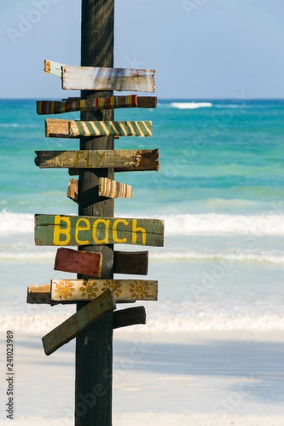 Fototapeta A signpost with Beach written on it with tropical beach and ocean in background on a sunny afternoon