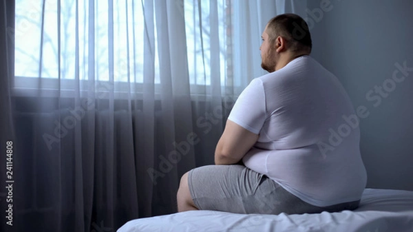 Fototapeta Sad heavy man sitting on bed at home, health problem, depression, insecurities