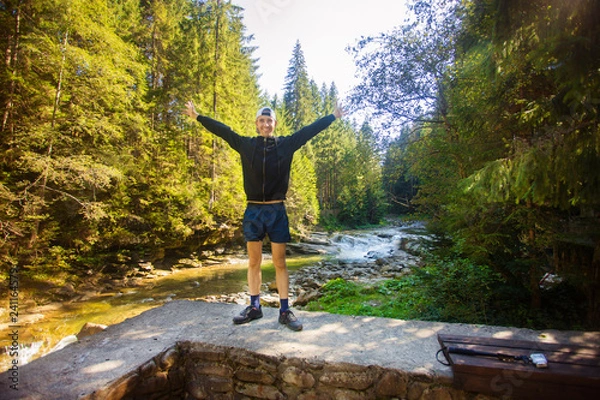 Fototapeta Young man walk near fast river in middle of forest