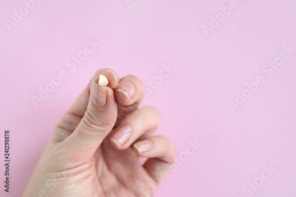 Obraz White woman palm holding first lost milk tooth on neutral pink background. Hand with little loose tooth. Kids dentistry. Miss children teeth in female fingers with selective focus.