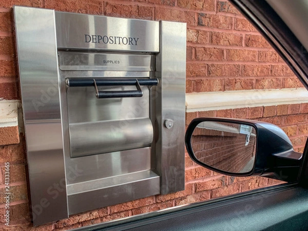 Fototapeta The 24-hour drive-thru night depository of a neighborhood bank set on a brick wall and seen through the car window in a horizontal image format.