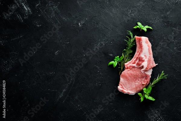 Fototapeta Raw steak on the bone. Meat with spices and herbs. On a black stone background. Top view. Free copy space.