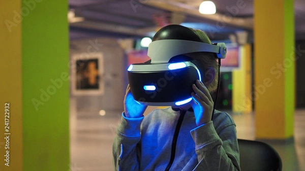 Fototapeta child sits in a large game room and looks at the glasses for virtual reality
