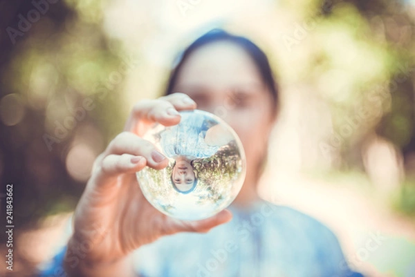 Obraz Beautiful woman hold crystal ball and can see a nice view that reflects through the big marble ball. Filtered image.