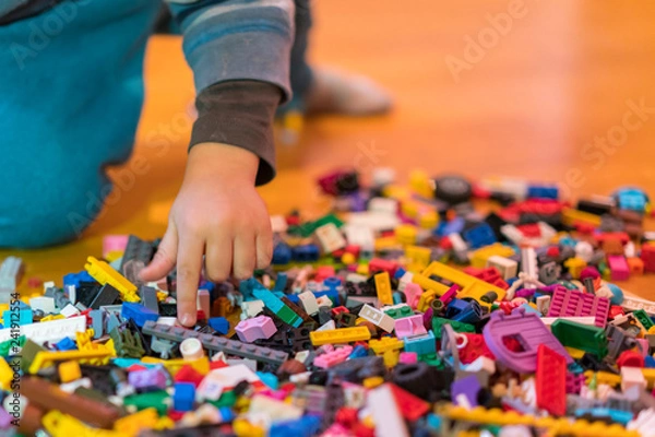 Fototapeta Close up of colorful plastic bricks on the floor. Early learning. Children's plastic constructor on the floor. Children's hands play a little constructor. vertical photo.