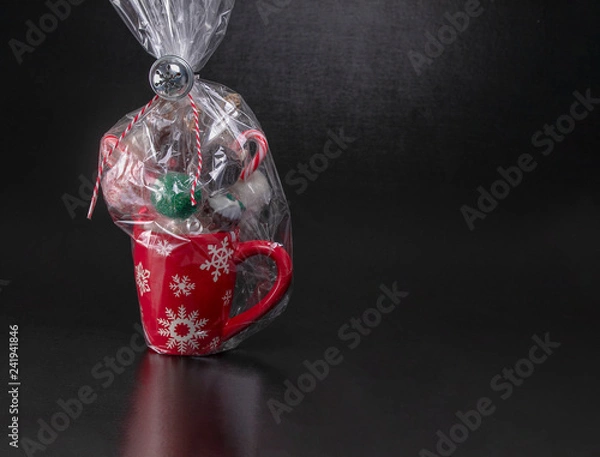 Obraz Wrapped red Christmas mug with snowflakes filled with cake pops, candy canes and marshmellows on a black background with text space.  Christmas gifts, baked gifts