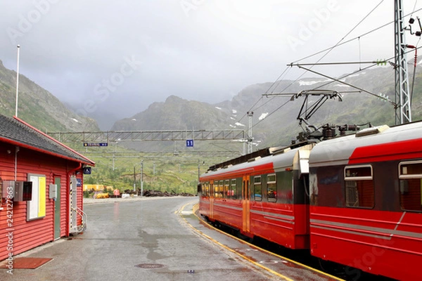 Fototapeta View of Voss mountain train stopped at Myrdal train station with snowy peaks on backgound, Norway.