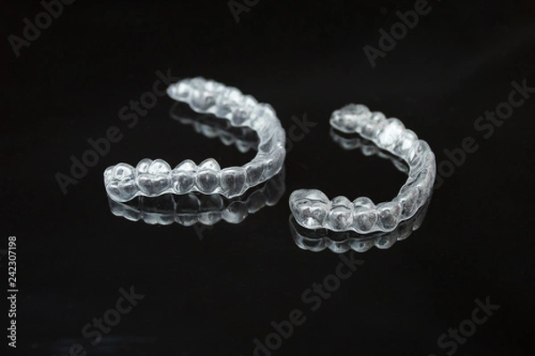 Obraz A pair of upper and lower clear retainers or aligners side by side on a dark reflective surface against a black background.
