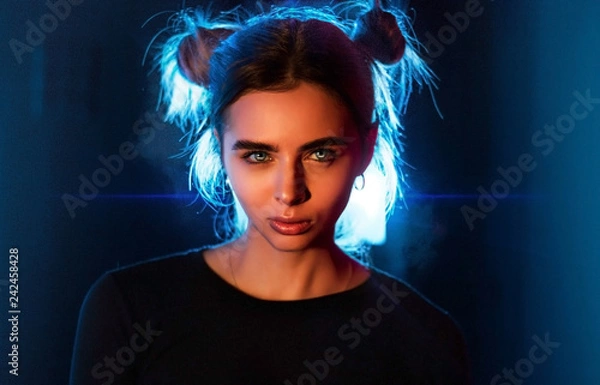 Obraz Close-up portrait of an angry angry girl in the studio on a dark background with neon backlight