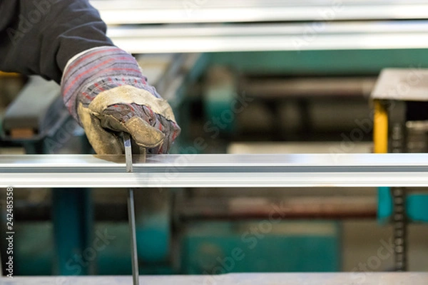 Obraz A man machine operator using safety gloves controlling the stretch of an aluminiun profile with a squad.