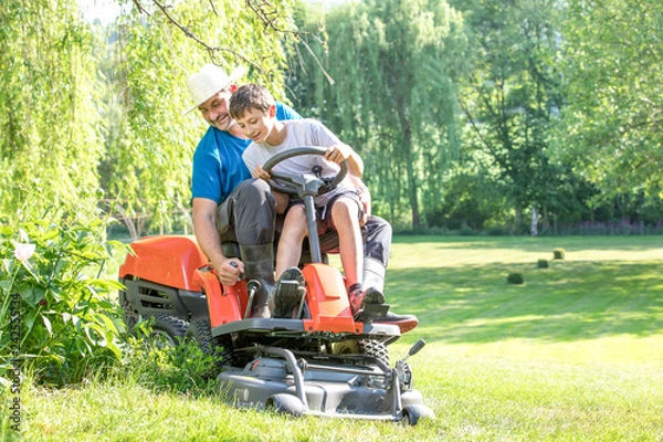 Obraz junger Mann, Vater mit Sohn mäht mit einem Rasentrimmer den Rasen Wiese im Sommer Frühling im grünen Garten