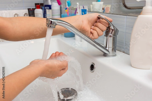 Fototapeta The child opens the faucet in the bathroom, and adjusts the warmth of the water