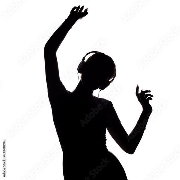 Fototapeta silhouette of a happy girl listening to music in headphones, figure of young woman with hands up relaxing on a white isolated background and dancing to the music