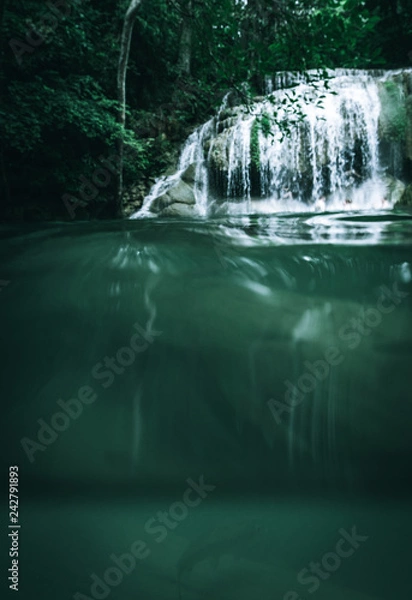 Fototapeta A waterfall taken from below the water with a fish in the foreground and the waterfall in the background within a beautiful jungle in Thailand in Asia in a healthy natural environment