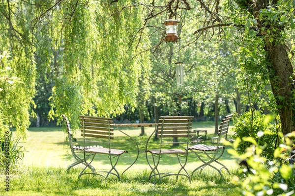 Obraz young pretty blond woman with long hair enjoys her free time in the green garden in spring summer sitting at a wooden hut on a bench, with a ship's lamp