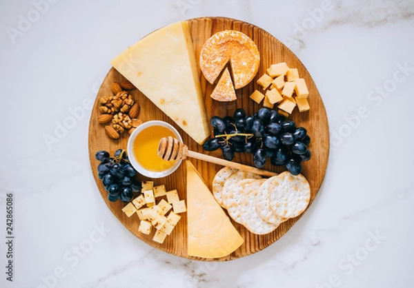 Fototapeta Flat lay with various types of cheese, grapes, nuts, honey and cracker in wooden board on marble