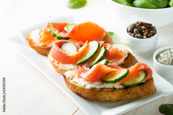 Obraz Salmon, cucumber and cream cheese bruschetta. Italian tapas, antipasti with vegetables, herbs and oil on grilled ciabatta and baguette bread. Sandwich.