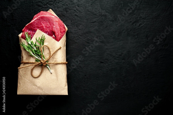 Fototapeta meat from a butcher shop, wrapped in paper. A piece of beef on a concrete black background