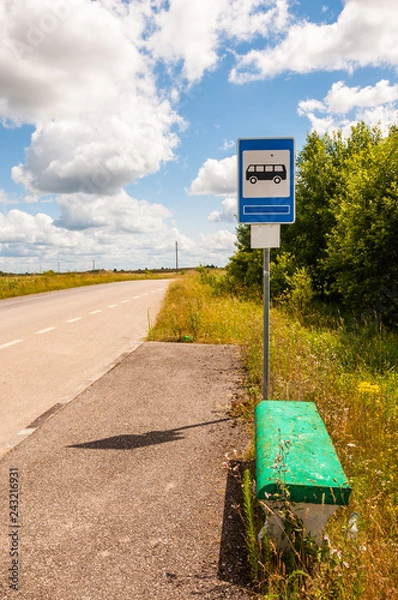 Obraz Old fashion bus stop with painted green concrete bench on country road surrounded by rural nature, fields and plants