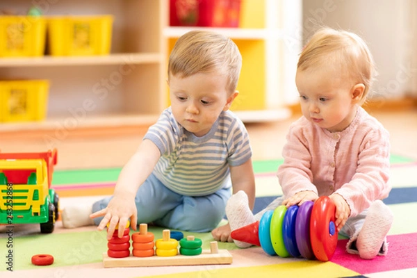 Fototapeta Przedszkola chłopiec i dziewczynka gra na podłodze z zabawkami edukacyjnymi. Małe dzieci w domu lub w przedszkolu.