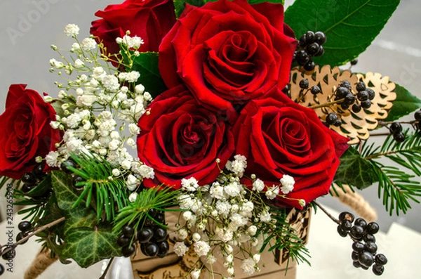 Fototapeta Bouquet of red roses, surrounded by sprigs of white gypsophila,berries, and conifer twigs in a small wooden box





