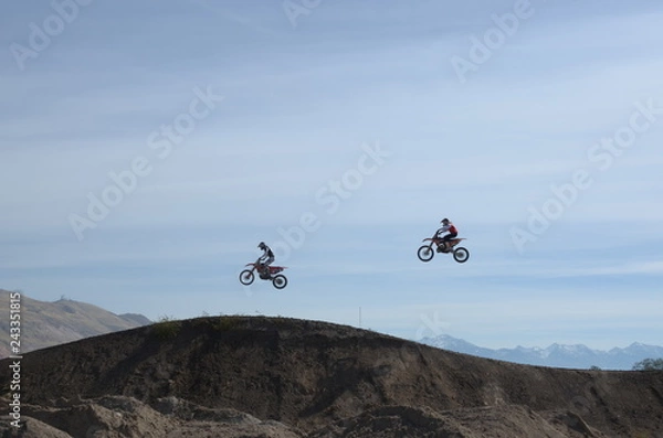 Obraz Two motocross riders in mid jump, side view at dirt track.
