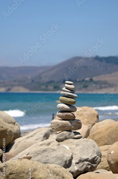 Fototapeta Stack of rocks at the beach with ocean and mountain background.