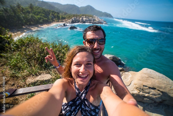 Fototapeta happy couple taking selfie photo in front of the sea in Tayrona National Park, Tropical Colombia. Crazy tourists travelling on the white beach of caribbean sea. 