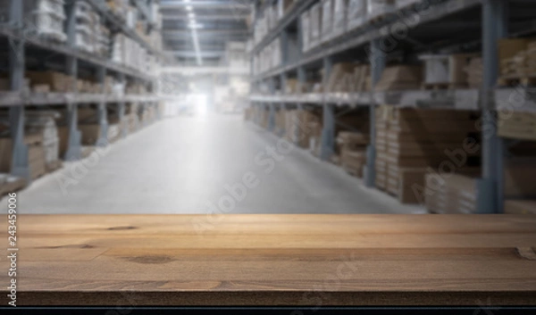 Fototapeta Wooden table top for product display montage. Blured shelves with goods in store at factory warehouse storage in the background. Stock concept.