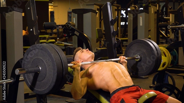 Fototapeta Strong man doing exercises with barbell in gym