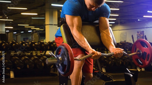 Fototapeta Man athlete trainer showing how to make excersis on biceps