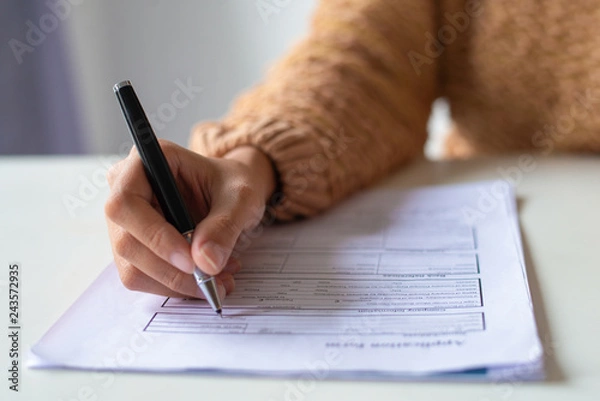 Obraz Zbliżenie pani wypełniającej formularz zgłoszeniowy. Nie do poznania kobieta w swetrze siedzi przy stole i przygotowuje CV. Koncepcja poszukiwania pracy