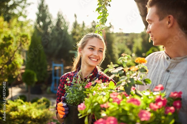Fototapeta Gardeners happy boy and girl hold pots with plants in beautiful gardens on a warm sunny day
