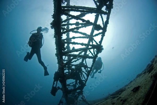 Fototapeta Scuba Divers on a ship wreck in clear blue water with sun in the background