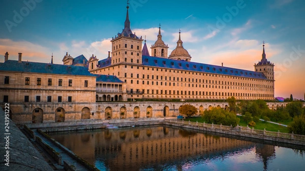 Fototapeta Sunset behind the beautiful El Escorial palace and monastery at the San Lorenzo de El Escorial with the Frailes Garden and reflections in the pond. Famous kings residence near Madrid in Spain