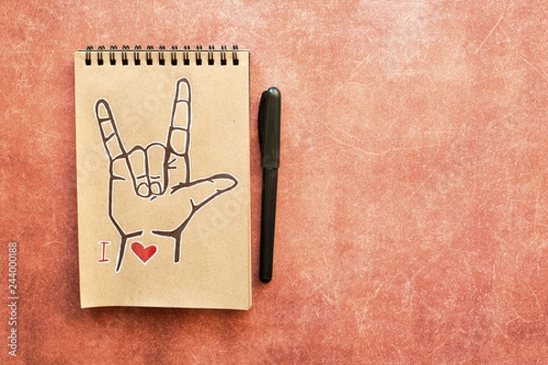 Fototapeta Notebook of Kraft paper, with a painted ASL (American sign language) symbol I Love you (ILY). Suitable for congratulations to the holiday Valentines day