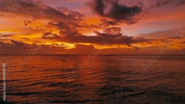 Obraz stunning beautiful aerial drone image of a red tropical sunset above the sea ocean with two man in a canoe fishing