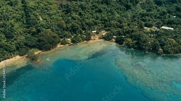 Obraz aerial drone image of a south pacific village on a remote island with a beautiful coral reef and lush tropical rainforest jungle while a small motor boat approaching
