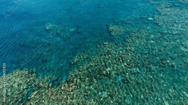 Obraz stunning aerial drone image of a a small fishing boat entering an a sea ocean anchorage in a channel next to a coral reef in crystal clear azure blue water at a remote isolated tropical island