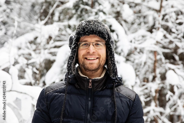 Obraz Man in fur winter hat with ear flaps smiling portrait. Extreme in the forest