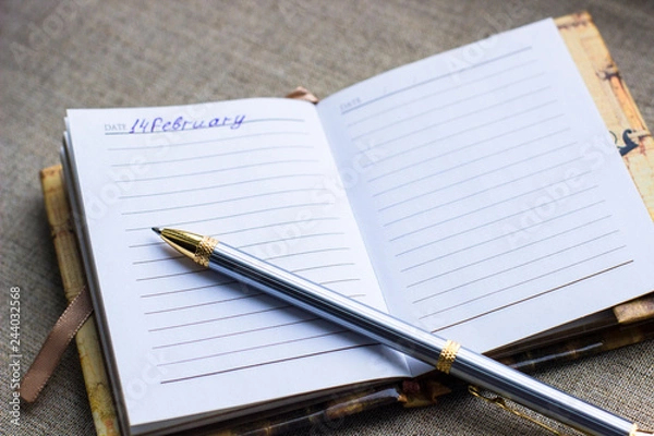 Fototapeta Valentines day background- silver pen are on the page of the diary on grey matting background, top view, flat lay, copy space. Mothers day, other celebration or planning and dream concept. 