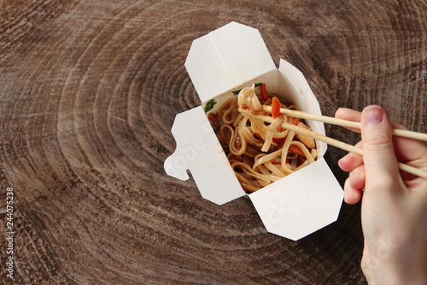 Fototapeta Udon Japanese noodle. female hand using chopsticks. wok with chicken and vegetables