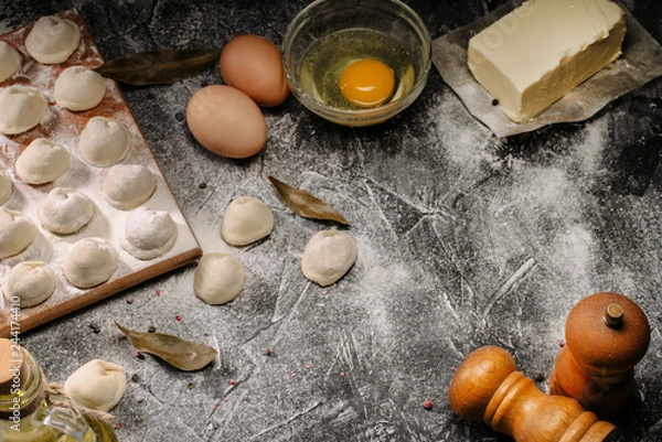 Fototapeta Homemade pelmeni, ravioli, dumplings with meat. Flour, eggs, fresh dough on a black background. Top view