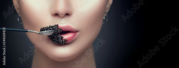 Obraz Piękna moda modela kobieta je czarnego kawior. Piękno dziewczyna z kawiorem na jej wargach odizolowywać na czarnym tle