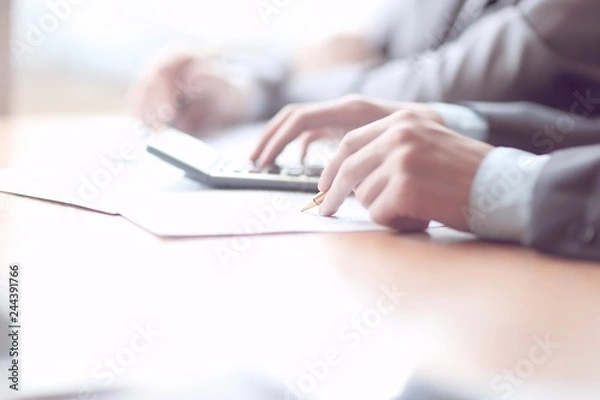 Fototapeta Close up of businessman or accountant hand holding pencil working on calculator to calculate financial data report,