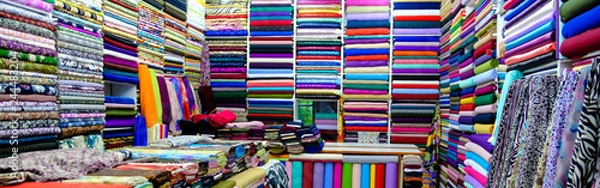 Fototapeta clothes in shop, Rolls of fabric and textiles for sale stacked on shelves in shop, View of cloth rolls of different colors and patterns on shelves in fabric store