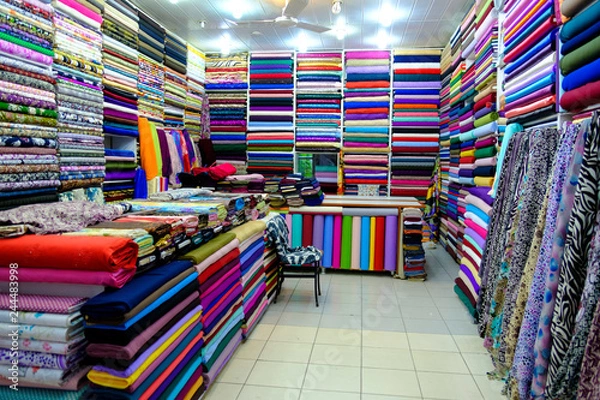 Fototapeta Rolls of fabric and textiles for sale stacked on shelves in shop,View of cloth rolls of different colors and patterns on shelves in fabric store 