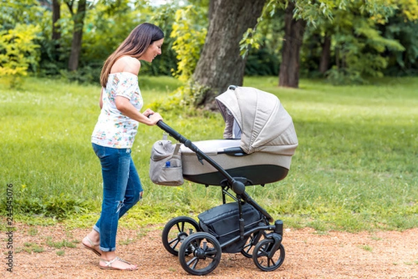 Obraz A beautiful young mother walking with her baby in a stroller in the park on a sunny day.