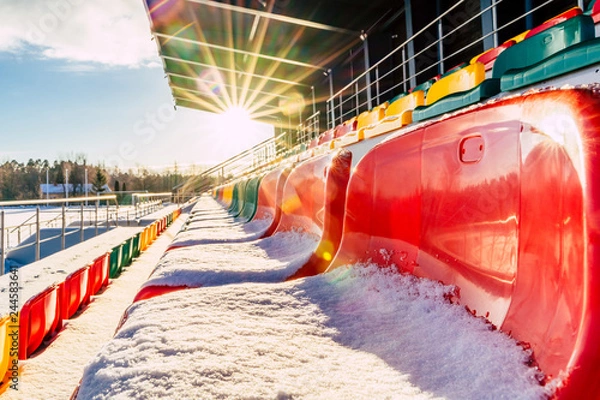Fototapeta Empty Colorful Football (Soccer) Stadium Seats in the Winter Covered in Snow - Sunny Winter Day with Sun Flare