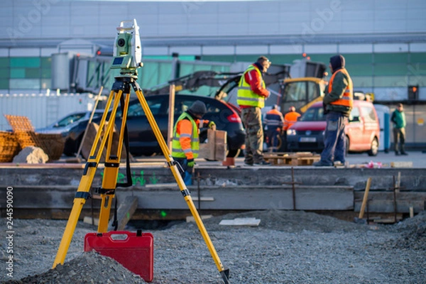 Fototapeta Surveyor equipment (theodolite) on construction site of the airport, building or road with construction machines in background